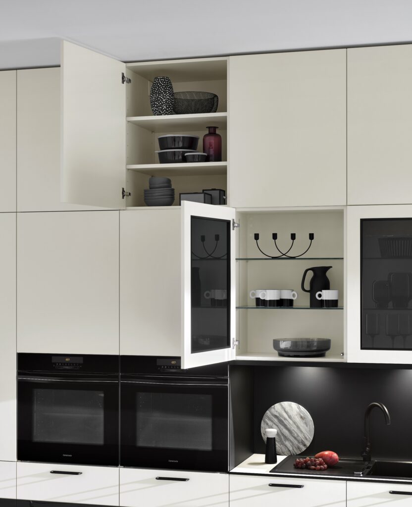Modern kitchen with white cabinets, some of which are open for organizing cabinets for easy reach. Inside are various dishes and decorative items. Below the cabinets are two black built-in ovens and a black backsplash with decor. Modern kitchen with white cabinets, some of which are open for organizing cabinets for easy reach. Inside are various dishes and decorative items. Below the cabinets are two black built-in ovens and a black backsplash with decor.