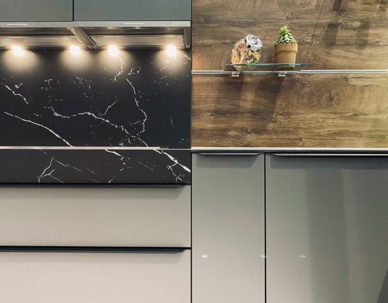 Modern kitchen design trends include a black marble countertop, wooden flooring, and gray cabinets, featuring under-cabinet lighting and decorative items on a shelf.